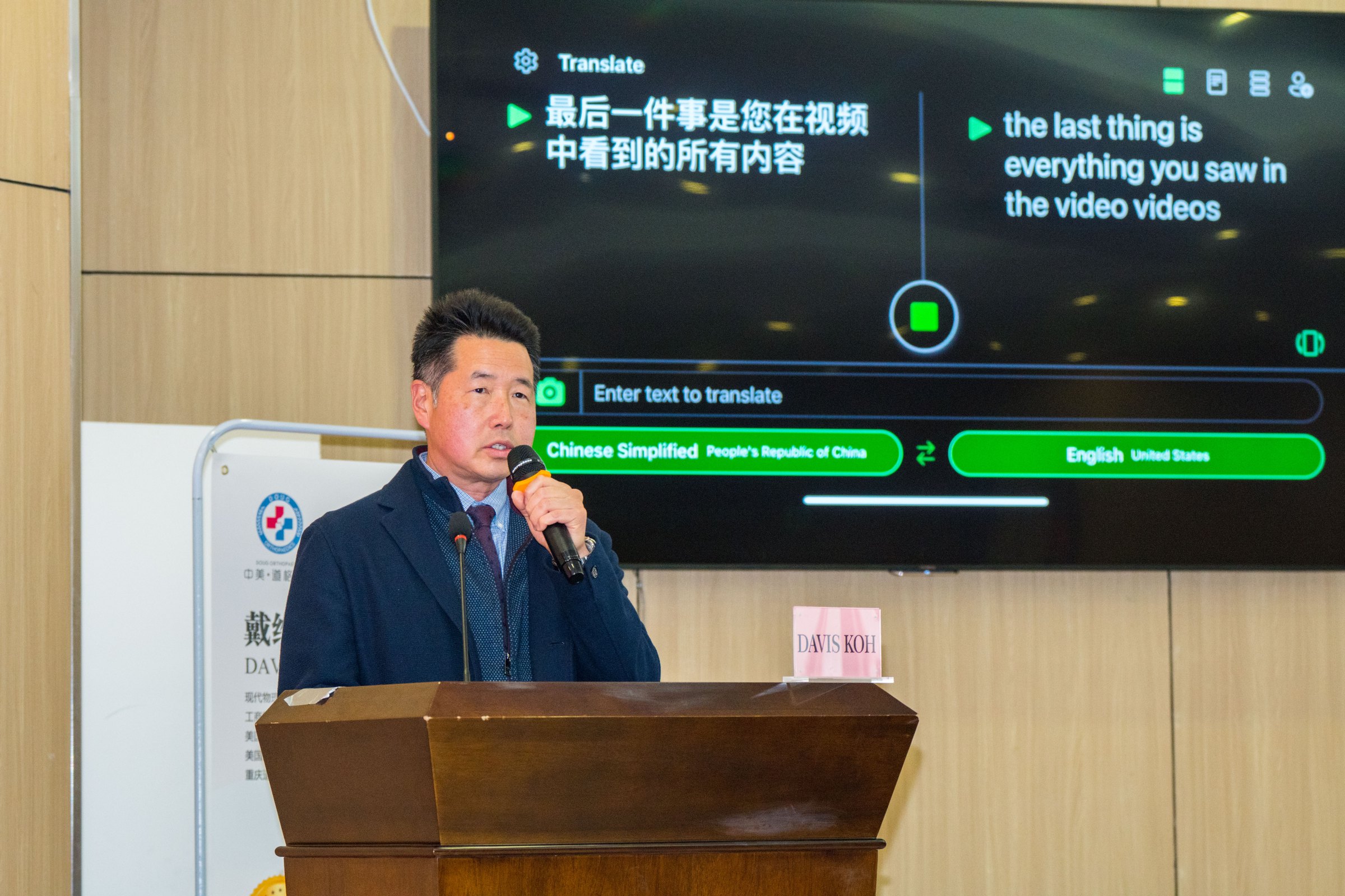Dr. Koh in a suit, speaking into a microphone at a wooden lectern