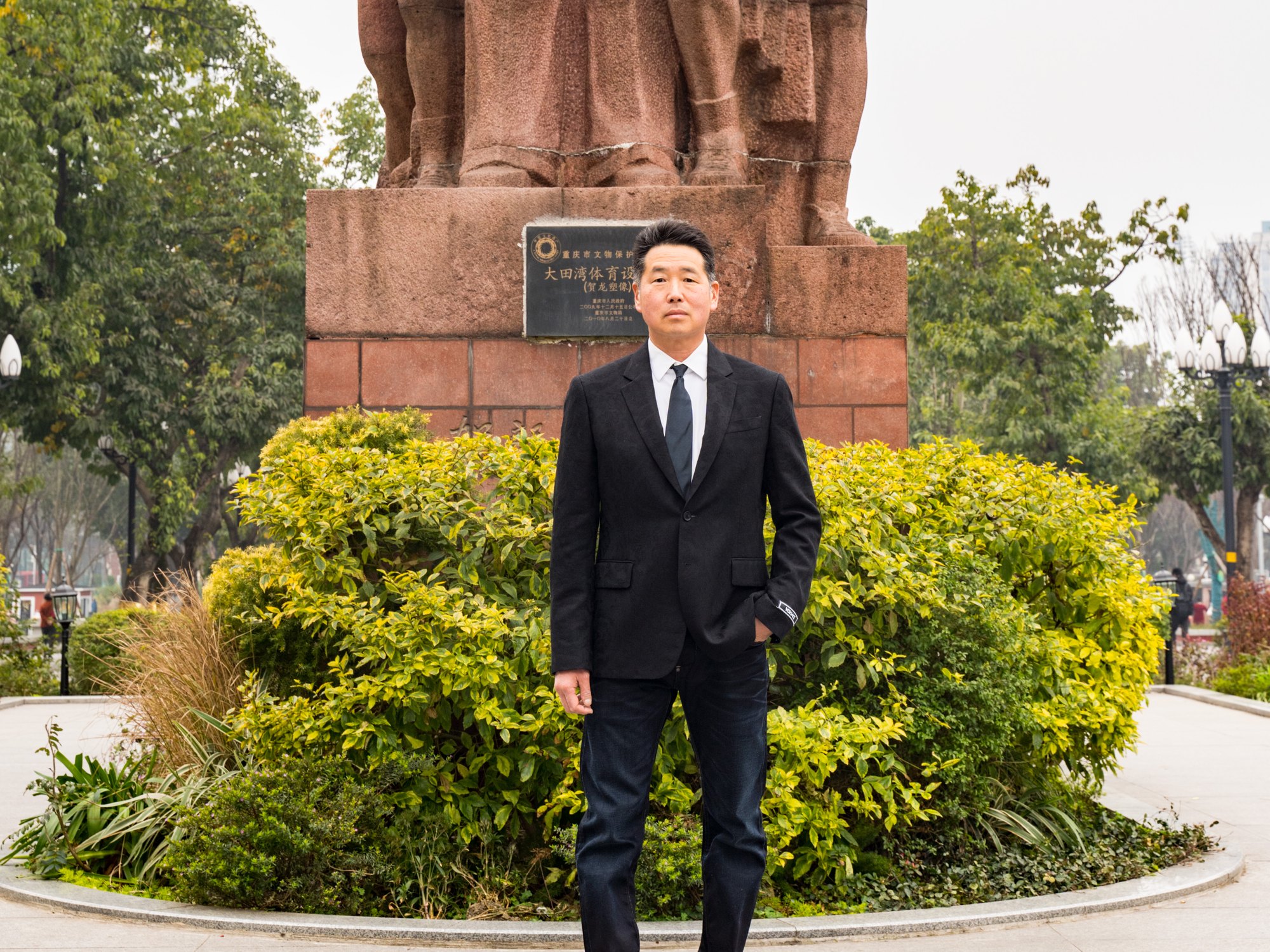Davis Koh in a dark suit, standing outdoors in front of a landscaped garden