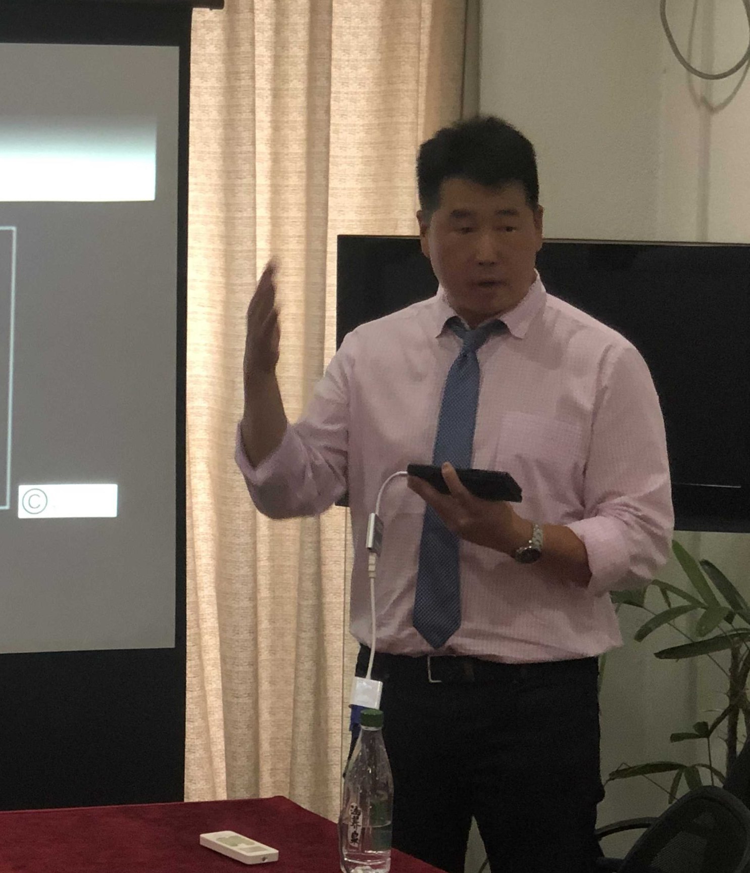 Dr. Koh in a shirt and tie, teaching beside a projector screen